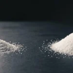 Two heaps of identical white powder on a dark surface, the left one visibly smaller, showing how much less glycine a magnesium glycinate dose delivers than the 3 g studied dose