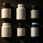 Six unlabelled supplement bottles laid out in two rows on a dark slate surface, their blank label panels facing up