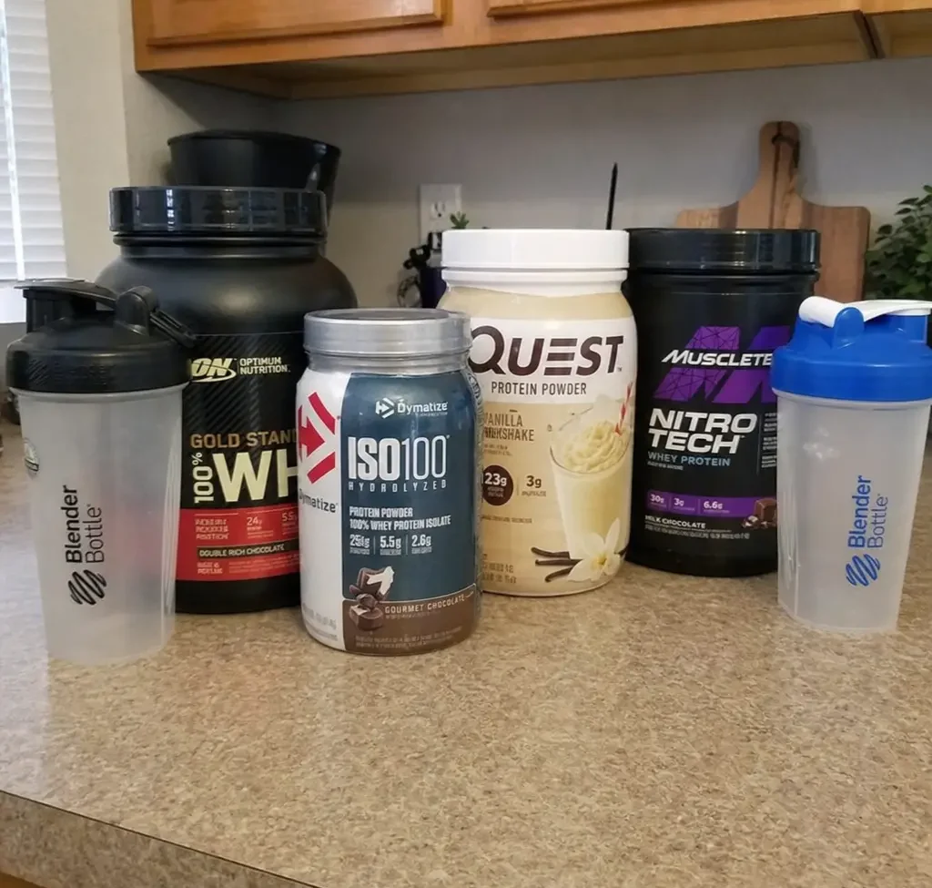 Assorted protein powder tubs and shakers lined up on a kitchen counter