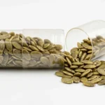 An open supplement capsule with pumpkin seeds spilling out of it onto a white surface, showing that the zinc in a sleep supplement is the same zinc found in food